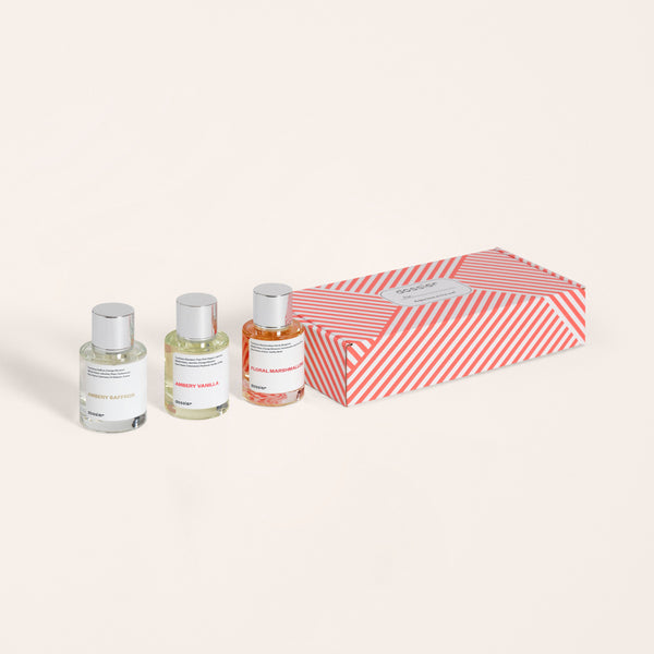 A set of three Dossier perfume bottles next to their red and white striped packaging box.