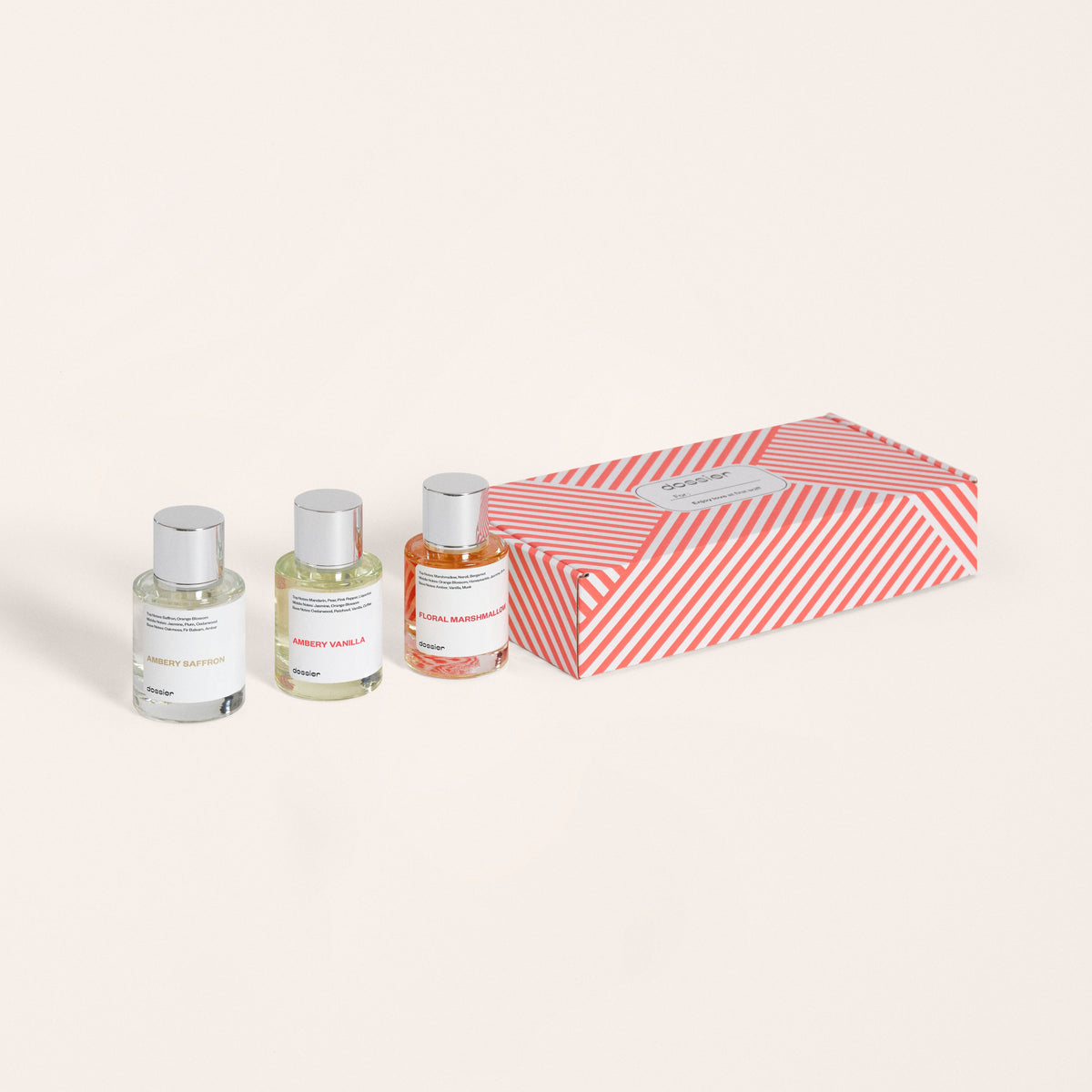 A set of three Dossier perfume bottles next to their red and white striped packaging box.